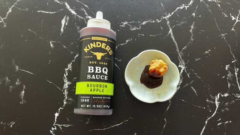 Kinder's bourbon apple BBQ sauce bottle next to sauce and chicken nugget on plate