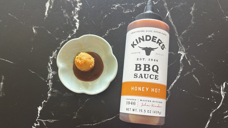 Kinder's honey hot BBQ sauce bottle next to chicken nugget and sauce on plate