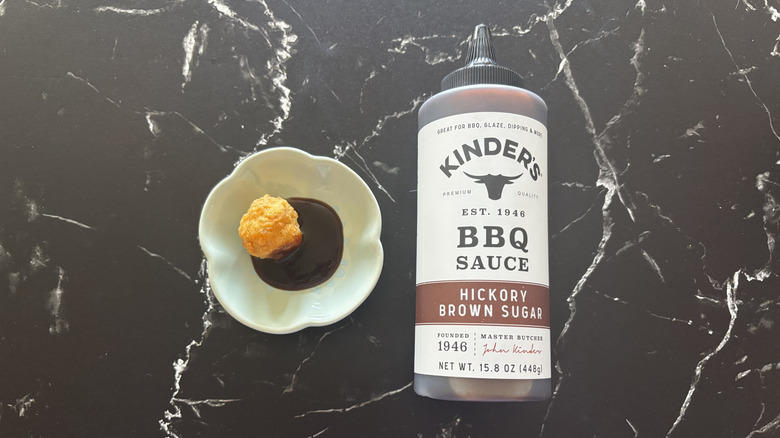 Kinder's hickory brown sugar BBQ sauce bottle next to chicken nugget and sauce on plate