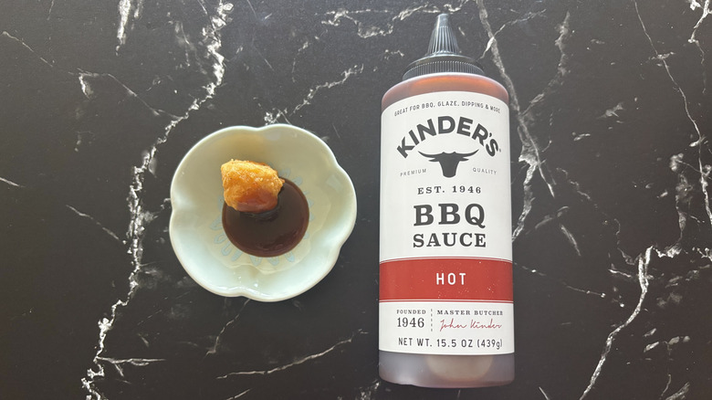 Kinder's hot BBQ sauce bottle next to chicken nugget and sauce on plate