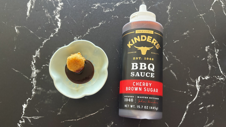 Kinder's cherry brown sugar BBQ sauce bottle next to chicken nugget and sauce on plate