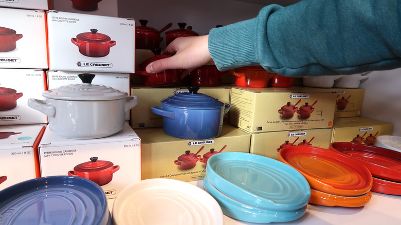 Customer reaching for Le Creuset display counter with cocottes and plates