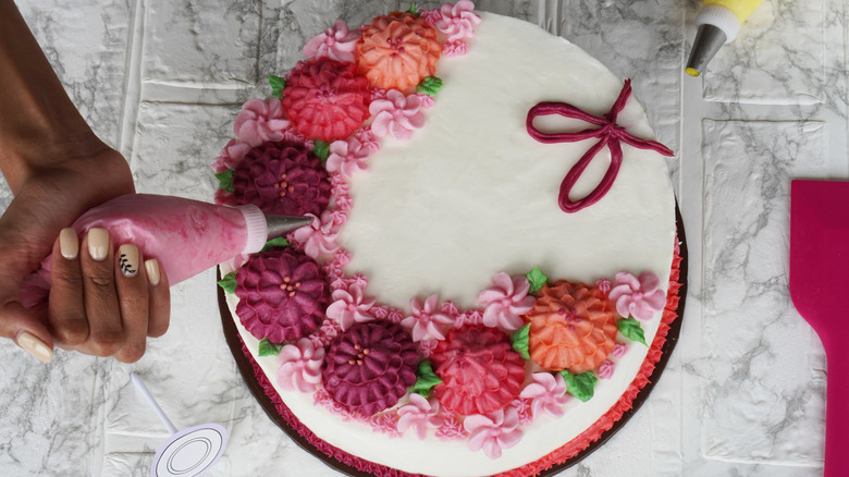 Hand piping icing in the shape of flowers onto round cake