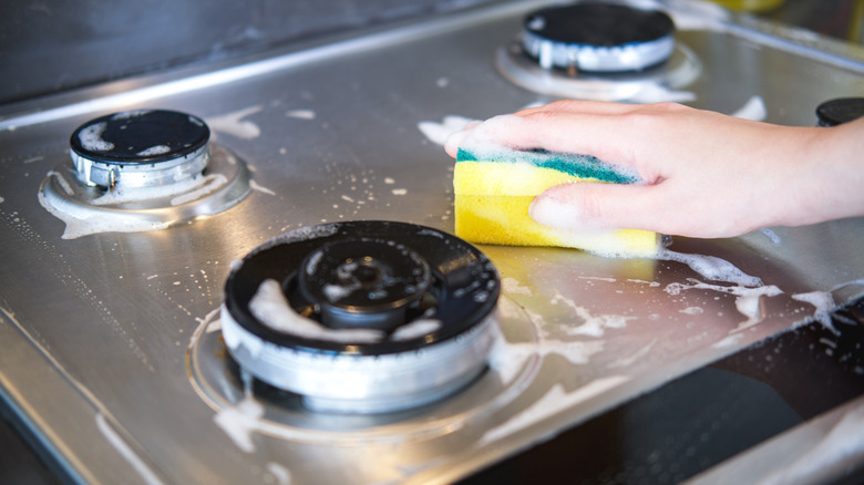 Hand cleaning gas stove with soapy kitchen sponge