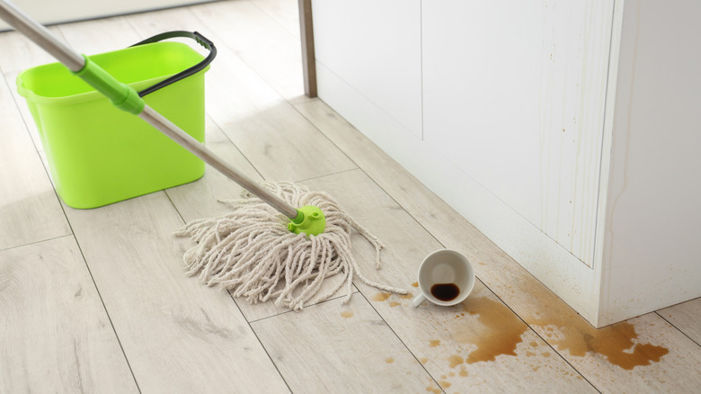 Overturned cup with spilled coffee and mop on kitchen floor