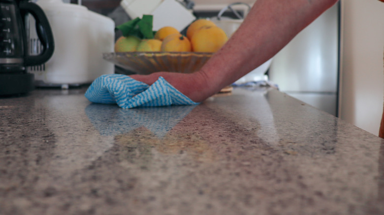Hand wiping down kitchen countertop with a cloth with appliances and lemons in the background