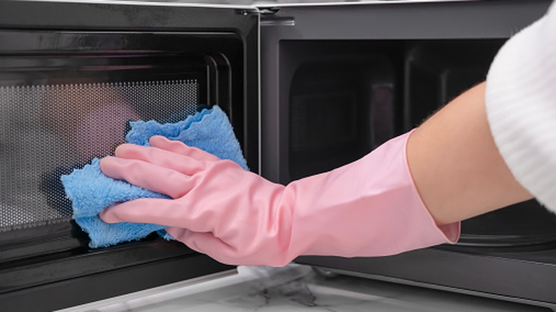 Hand wearing pink gloves and cleaning the door of a microwave