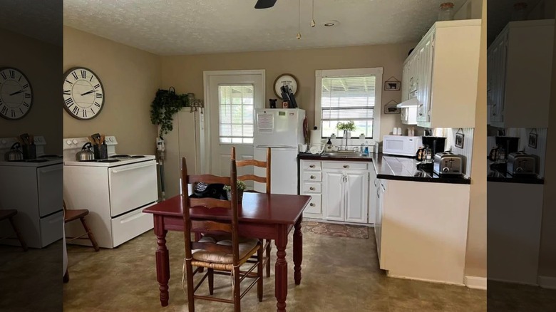 A rustic kitchen with white cabinets, wooden table and black tiled countertops
