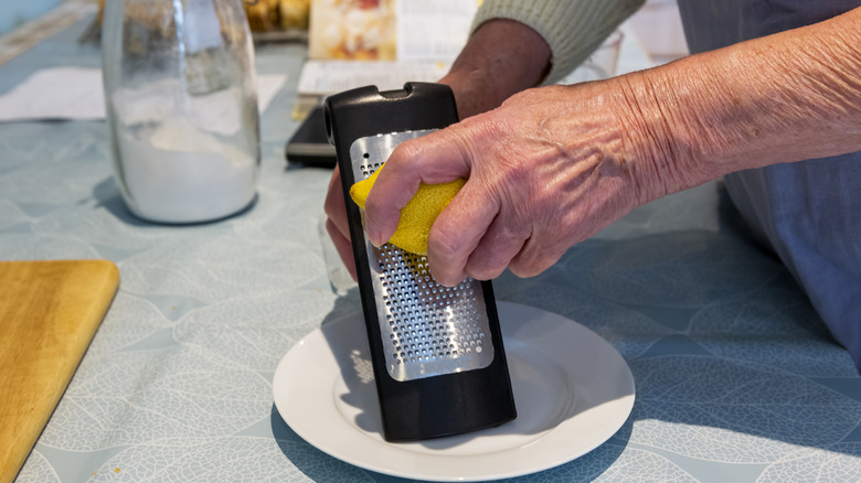 Hand rubbing lemon on a food grater to make lemon zest