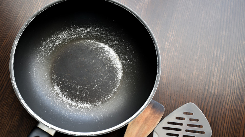 Scratched non-stick pan placed on table with ladles and spatulas