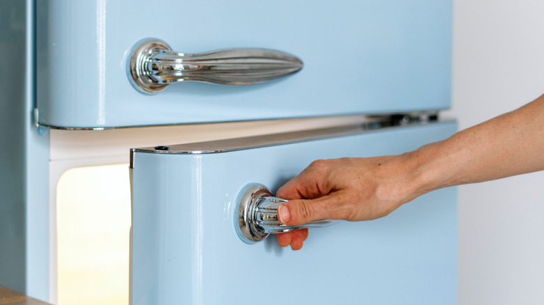 Hand opening blue fridge door with chrome handle
