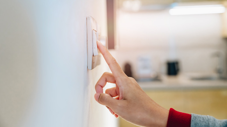 Finger touching light switch on wall in kitchen