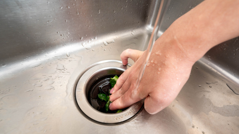 Hand pushing food waste into garbage disposal