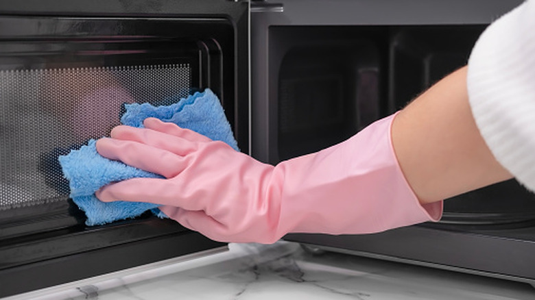 Gloved hand cleaning microwave door with cloth