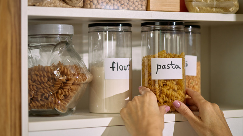 Hand reaching for a jar of pasta from a neatly organized pantry