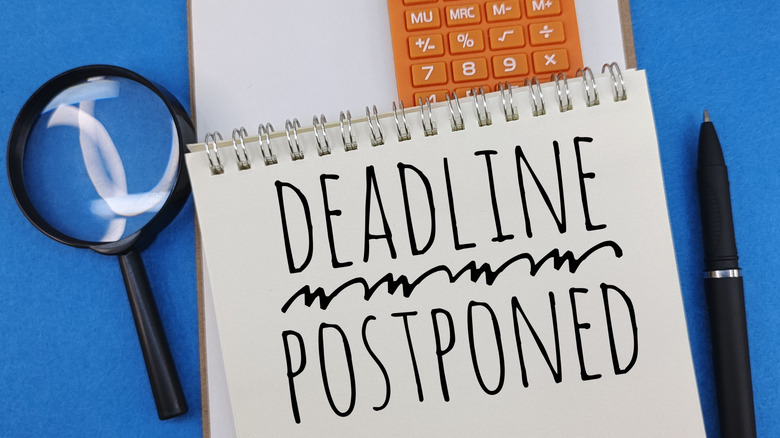 Deadline postponed written on a notepad against a blue background