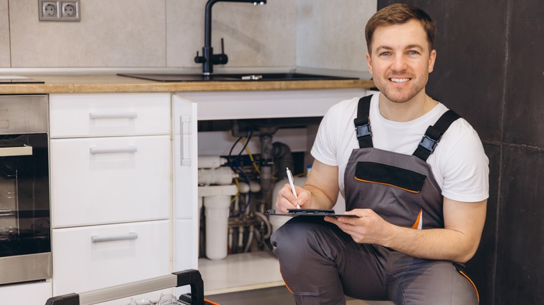 Construction worker in overalls sitting with a clipboard in front of a kitchen sink