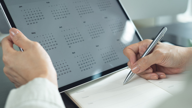 Woman looking at a monthly calendar on a tablet and making notes