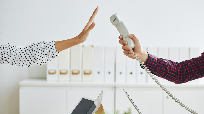 Man holding corded phone handset and woman gesturing stop