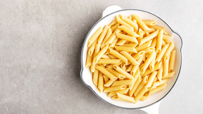 A white skillet full of plain cooked penne pasta sitting on a gray surface