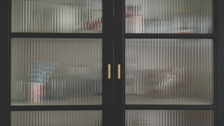 Dishware and kitchen essentials placed behind black doors with corrugated glass