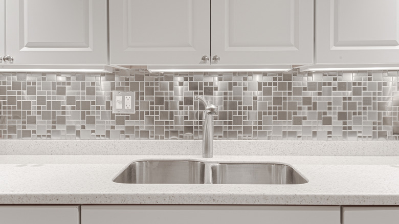 Kitchen interior with shiny backsplash, white cabinets and stainless steel faucet