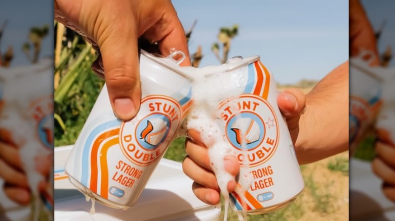 Hands clinking cans of Stunt Double Lager together outside
