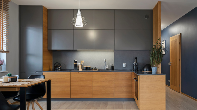 Kitchen interior with dark upper cabinets, grey walls, and wooden lower cabinets