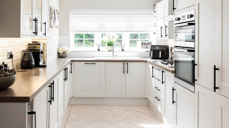 Interior view of a sunny white kitchen with wooden countertops and black hardware