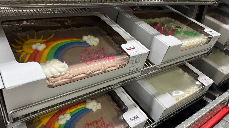 Half-sheet cakes with decorations like happy birthday packed in boxes and stacked on shelves inside a store