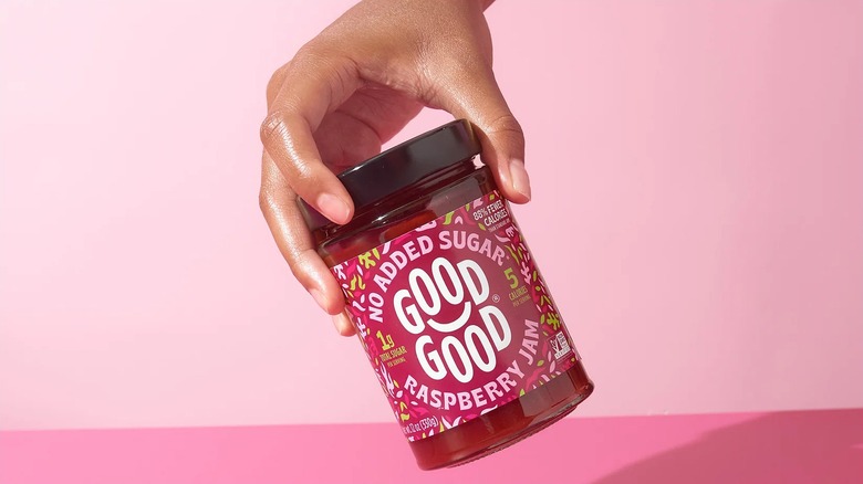 Hand holding jar of Good Good raspberry jam over pink background