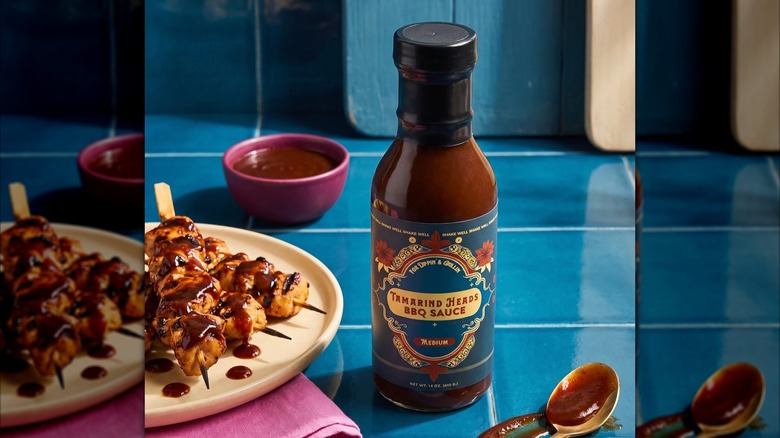 Bottle of Tamarind Heads BBQ sauce on blue counter, chicken kebabs on plate beside