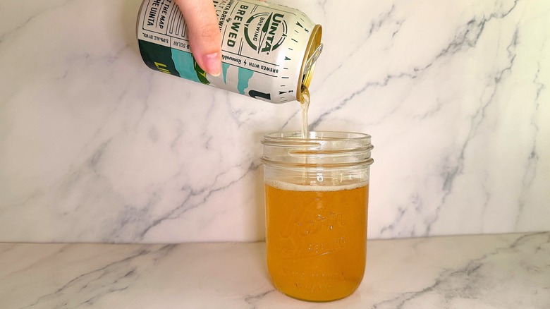 Hand pouring can of beer into glass on marble surface