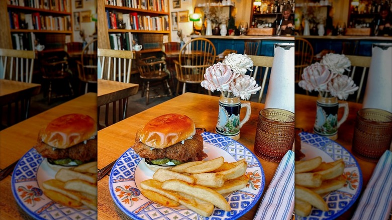 Fried fish sandwich and fries on table amidst restaurant filled with cottage decor and books