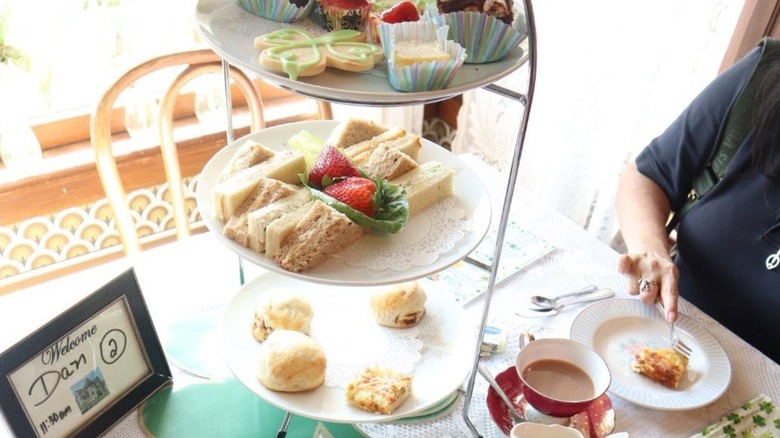 Tower of pastries, biscuits, and sandwiches on table with tea