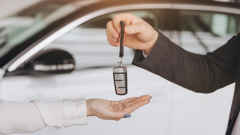 One person handing another person a car key in front of a car