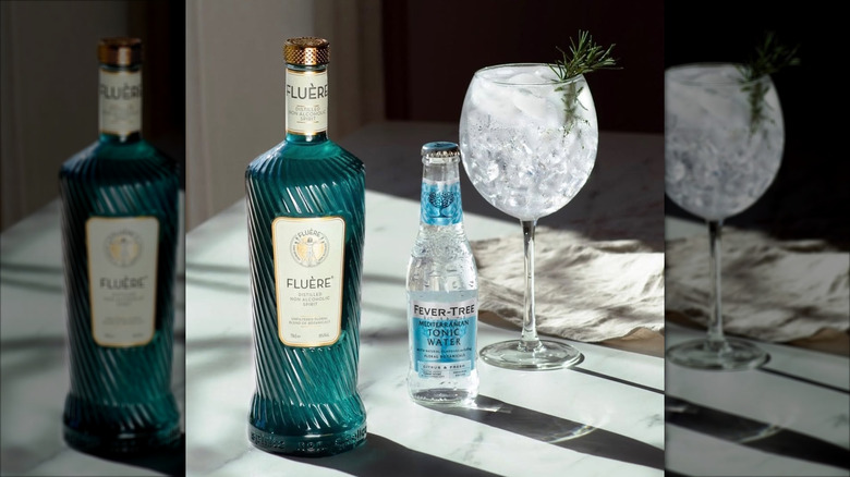 bottle of Fluère Botanical Blend gin with tonic and a tall glass filled with ice including a rosemary garnish