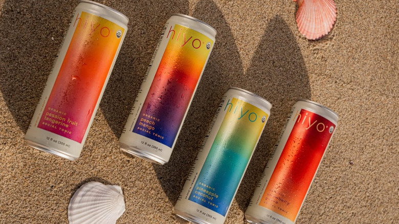 four cans of Hiyo non-alcoholic functional seltzers lying on sand