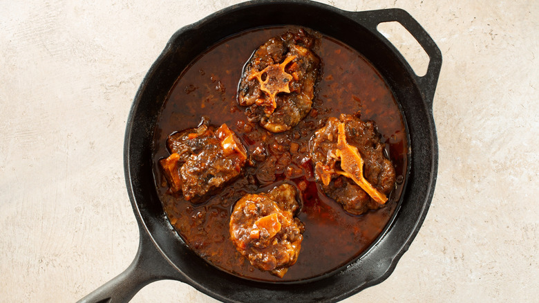 A topview of oxtail pieces braising in a pan