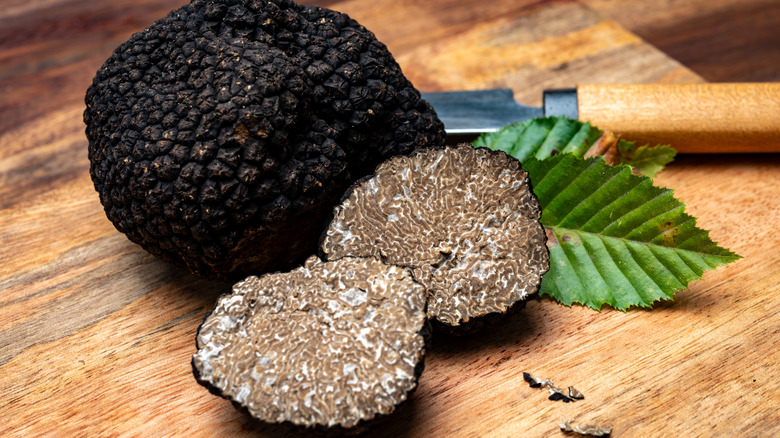 A whole black truffle with another black truffles sliced in half next to it