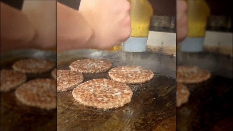 Using dispenser to add grill seasoning to burger patties cooking on griddle