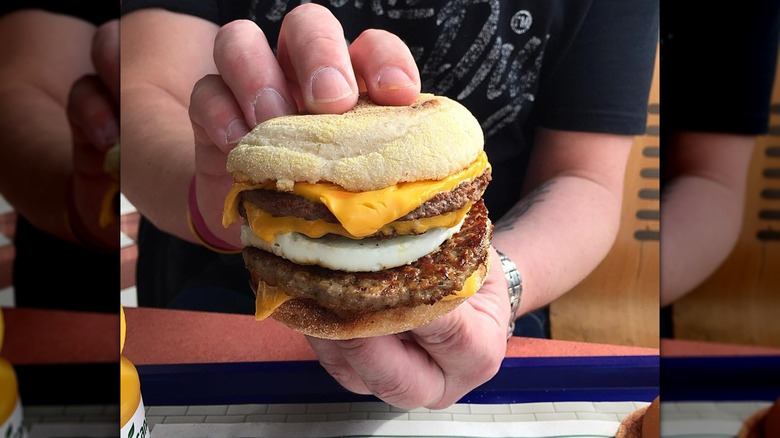 Hands holding McDonald's Mc10:35 McMuffin with beef patties, egg, and cheese