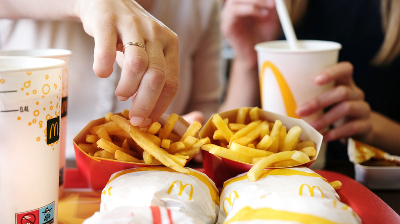 People reaching for McDonald's food on a tray in a restaurant