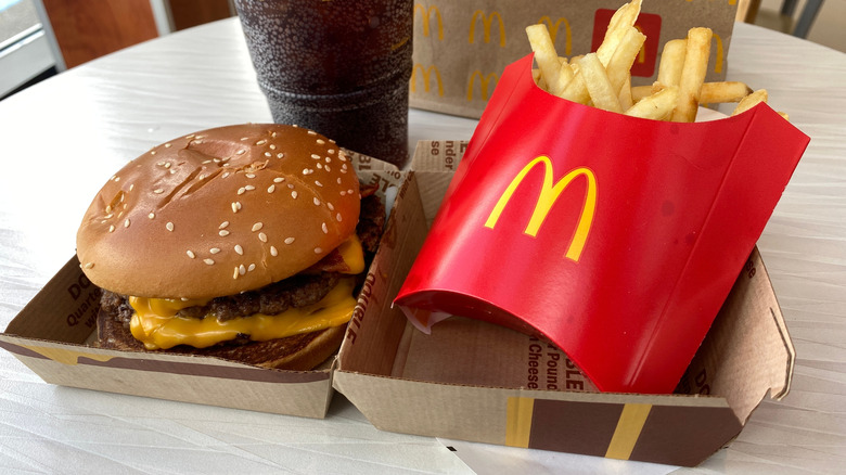 A McDonald's Quarter Pounder with cheese on a restaurant table with fries and a soda