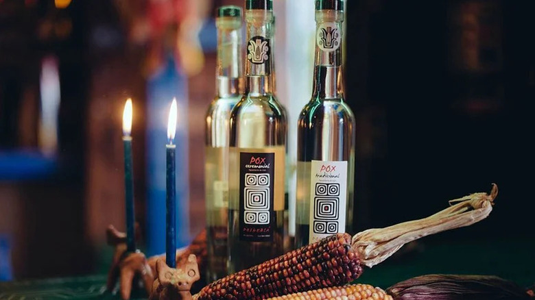 Bottles of Pox behind ancient corn and burning candles.