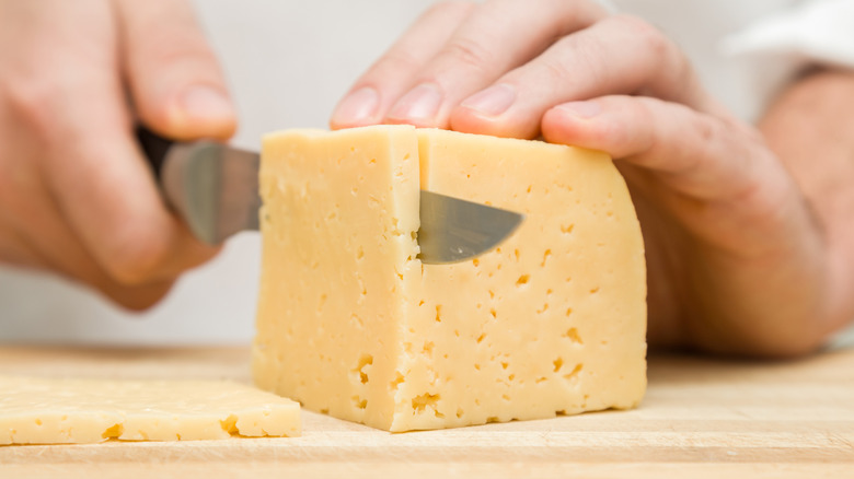 Hands cutting block of cheese on cutting board