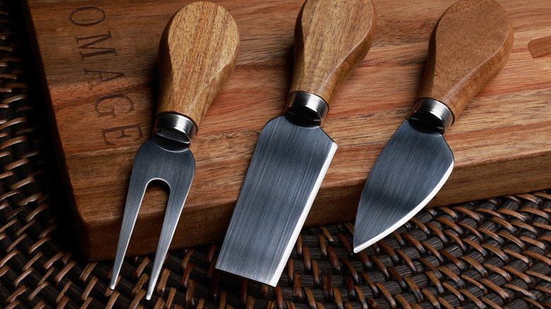 Three cheese knives on a wooden cutting board