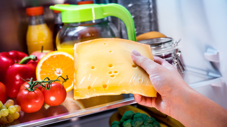 Hand removing block of cheese from fridge