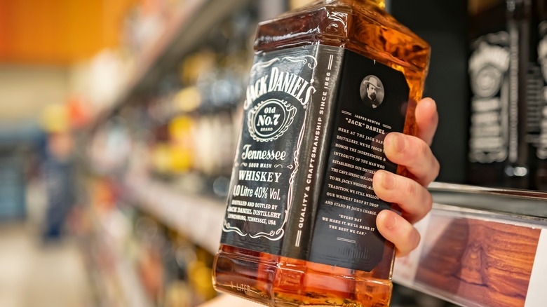 A close up of a person picking up a bottle of Jack Daniel's up from a store shelf