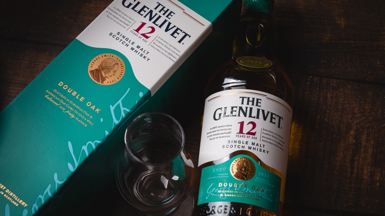 A bottle of The Glenlivet 12 alongside its packaging with an empty whisky glass in between them